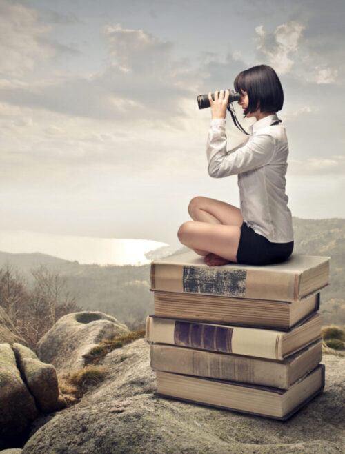 Woman sitting on books with binoculars